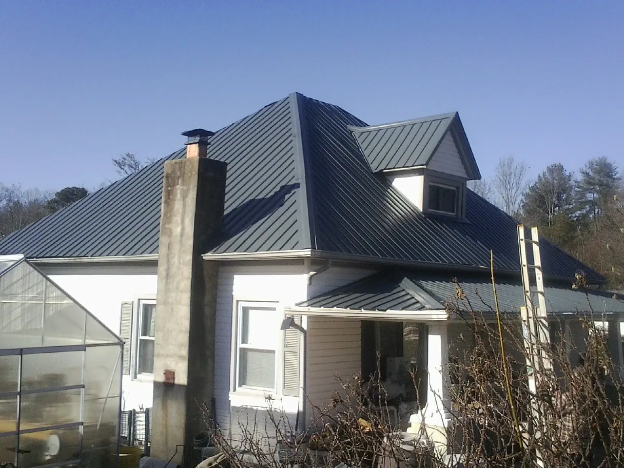 Dark blue standing seam metal roof on a white farmhouse with dormer — Slate & Tile Roof Repair by Roofing Brothers in Fair Play