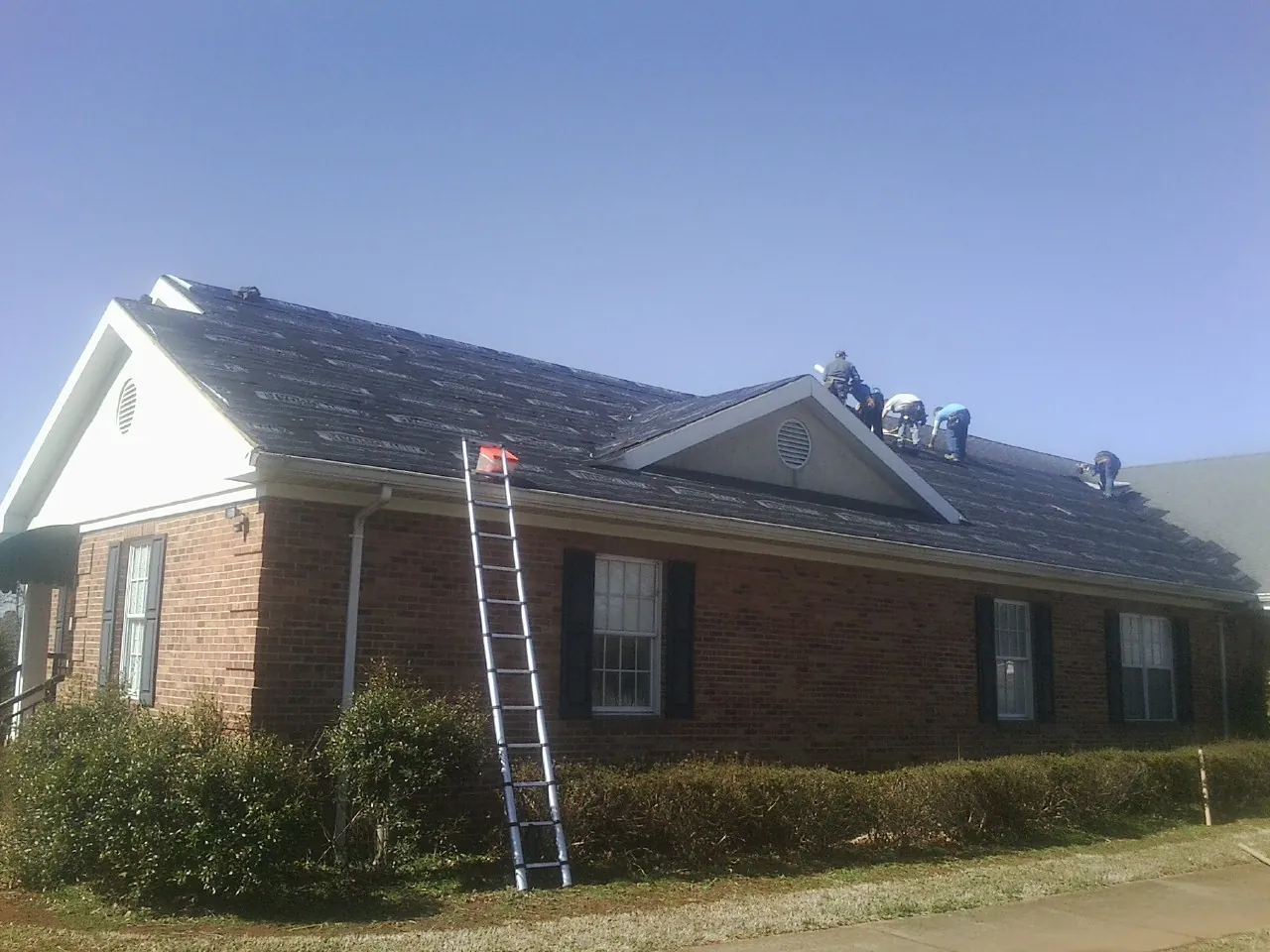 Crew tearing shingles off a brick ranch roof with a ladder set — Metal Roof Repair work by our crew in Fair Play