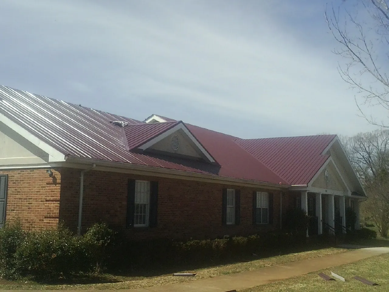 Red metal roof with gabled entries on a long brick building, from a Hail Damage Roof Repair job in Fair Play