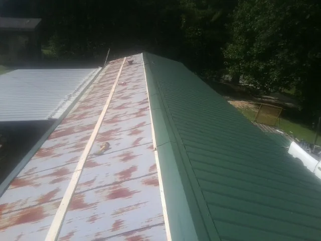Old rusted panels beside newly installed green metal roofing — Wind Damage Roof Repair by Roofing Brothers in Fair Play