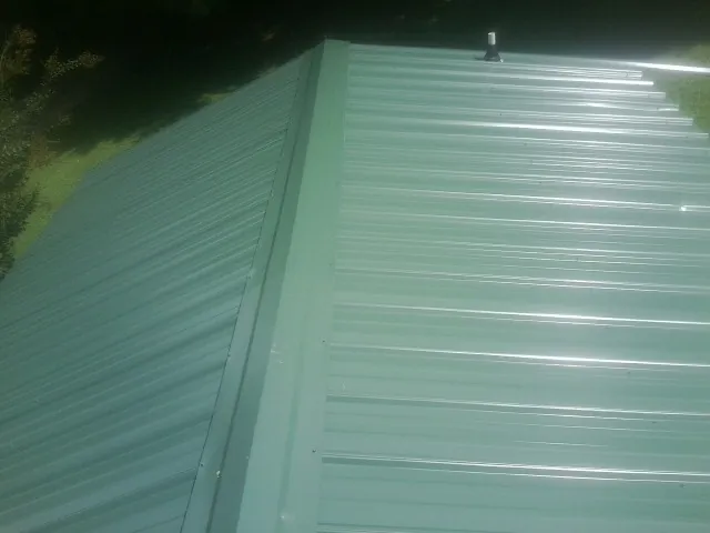 New green metal panels meeting at the ridge of a roof — Flat Roof Repair work by our crew in Fair Play