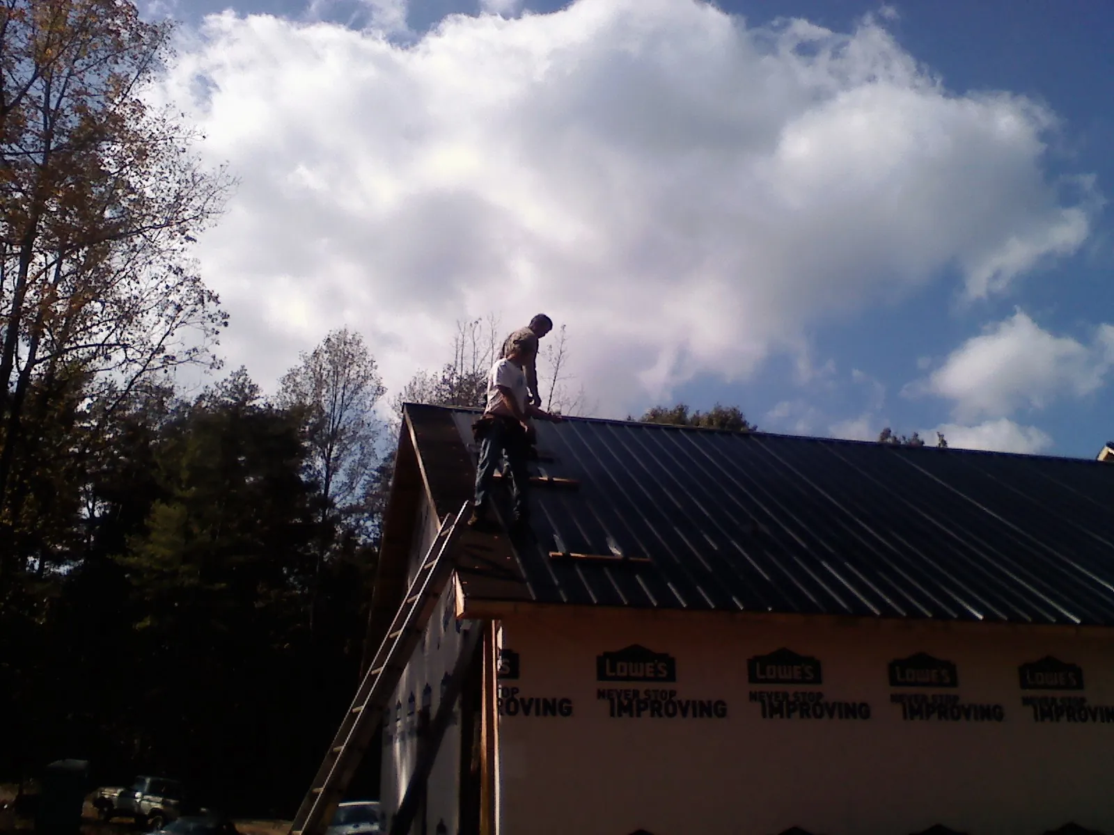 Roofer fastening dark metal panels high against a cloudy sky in Fair Play