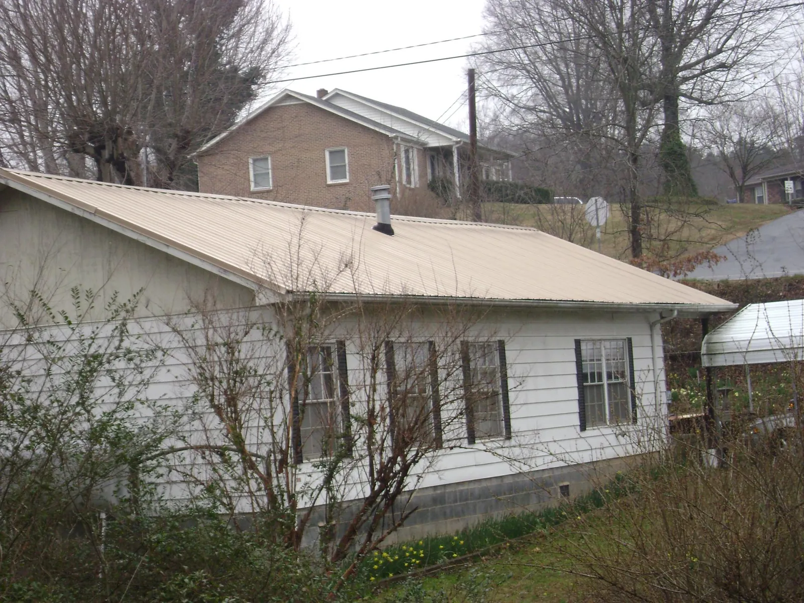 Tan metal roof on a white sided house set into a hillside — Commercial Roofing by Roofing Brothers in Fair Play